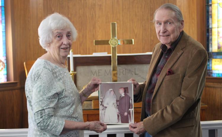 Megan Broome/The Clayton Tribune Catherine Turpen and Rev. James E. Turpen, Sr. stand in front of the altar at Tallulah Falls United Methodist Church and hold a picture from their wedding day where they said “I do” in the same spot  55 years ago on Dec. 20, 1964.