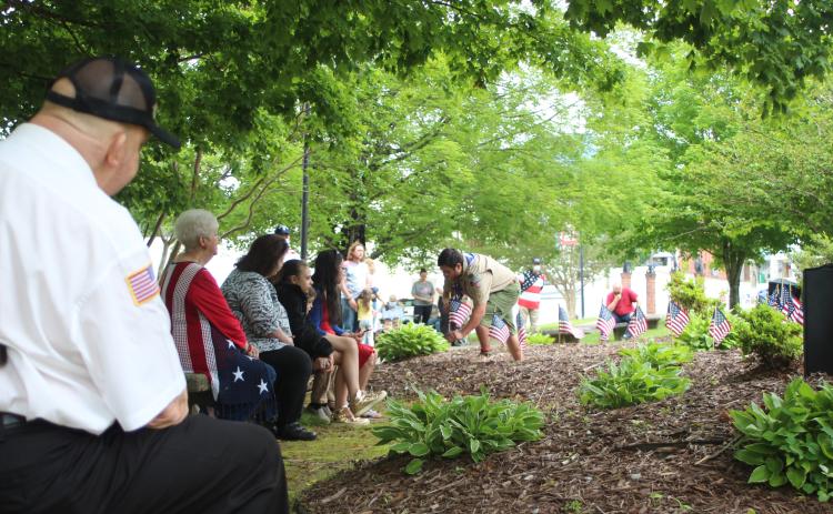 Megan Broome/The Clayton Tribune. Mickey Wood, left, and Francesca Franklin, along with members of the community watch as Dominic Cross places flags at the Veterans’ Monument in front of the Rabun County Courthouse as the names of all those in the armed forces who have passed away in the last year were read aloud.