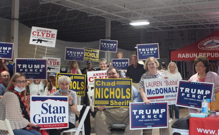 Megan Broome/The Clayton Tribune. Members of the Rabun County Republican Party and community patrons hold up campaign signs at the grand opening of their campaign headquarters last Saturday.