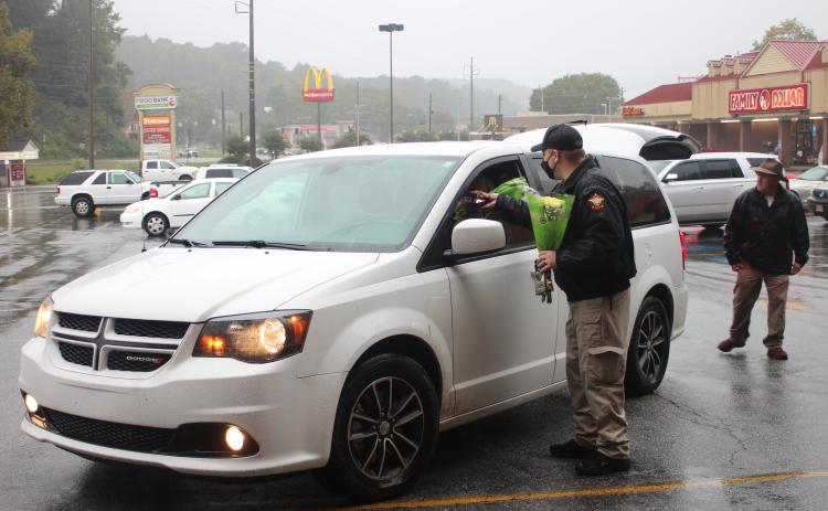 Megan Broome/The Clayton Tribune. Rabun County Detention Center Officer Daniel Nicholson hands out flowers and chocolate to families during the Faith and Blue food distribution event last Saturday. Each family was given these along with boxes of food.