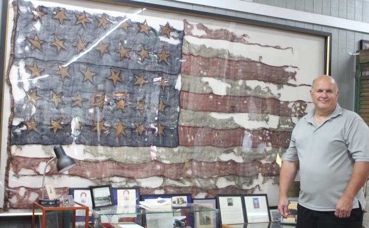 Megan Broome/The Clayton Tribune. Bob Matis, owner of Civil War Corner Antiques in Dillard, owns a United States flag used in the Civil War in the Battle of Cold Harbor on June 3, 1864. It is displayed in his shop along with a display. The flag has 34 stars and two stripes are missing after being torn off in battle.
