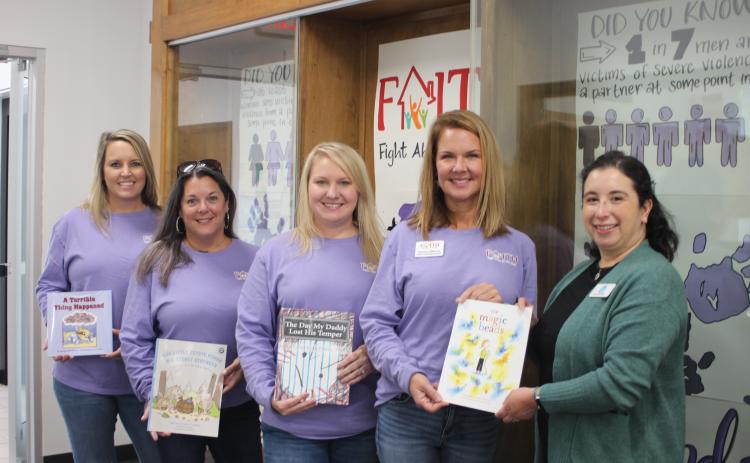 Megan Broome/The Clayton Tribune.  Brooke Cannon, grant administrator, left, Laura Davis, Empowering Families coordinator, Kayla Talley, FAITH legal advocate, Monica Blalock, director of community awareness, present books to Dyana Costello Banks, library manager, for donation to the Rabun County Public Library, in front of the library display.