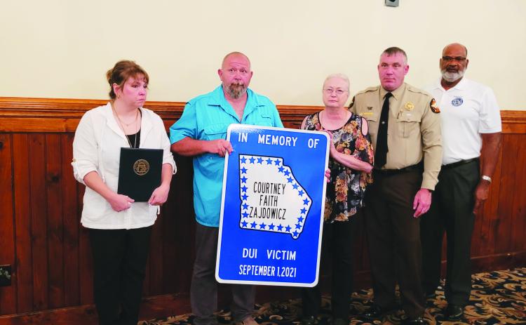 Photo by Megan Broome. Rabun County Sheriff Chad Nichols unveils a road sign honoring Rabun County Detention Center Officer Cpl. Courtney Faith Zajdowicz at the 31st annual Hands Across the Border event at The Dillard House Aug. 30. The sign will be erected at the crash site at George Eller Curve. Pictured are Courtney’s mother Crystal Zajdowicz, father David Cross, grandmother Janet Zajdowicz, Sheriff Chad Nichols and Allen Poole, director of the Georgia Governor’s Office of Highway Safety (GOHS).