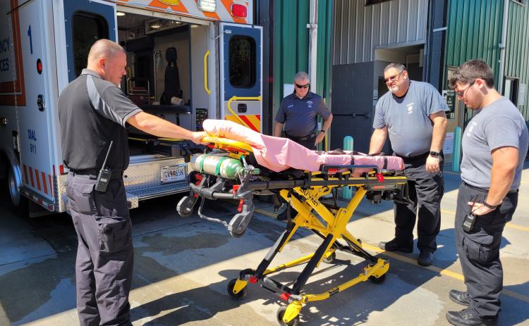 Megan Broome/The Clayton Tribune. Rabun County EMS Captain Trampes Stancil, EMS/911 Director Mike Carnes; Paramedic Don White and EMT Will Shanks demonstrate how the Stryker Power Load System automatic hydraulic lifting equipment lifts patients who are on stretchers in and out of the ambulance. This system significantly helps reduce workplace injuries.