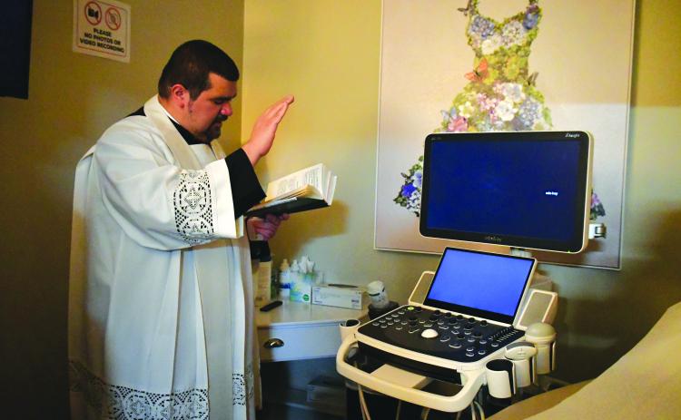 Megan Broome/The Clayton Tribune. Father Luis Alvarez blesses the new ultrasound machine.
