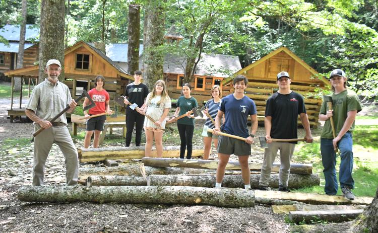 Megan Broome/The Clayton Tribune. Local students participate in the Foxfire Summer Leadership Program and help Foxfire Museum Director Barry Stiles hew logs to prepare building the miniature replica Blacksmith Shop that will be featured at The Children’s Village. Pictured are Stiles; Rabun County High School students Luke Thompson, Sam Flaherty, Celton Littrell, Sean Flaherty, Brinn Justice, and Gavin Sharpe; Rabun Gap-Nacoochee School student Lily Karplus; and home-schooled student Olivia Nixon.