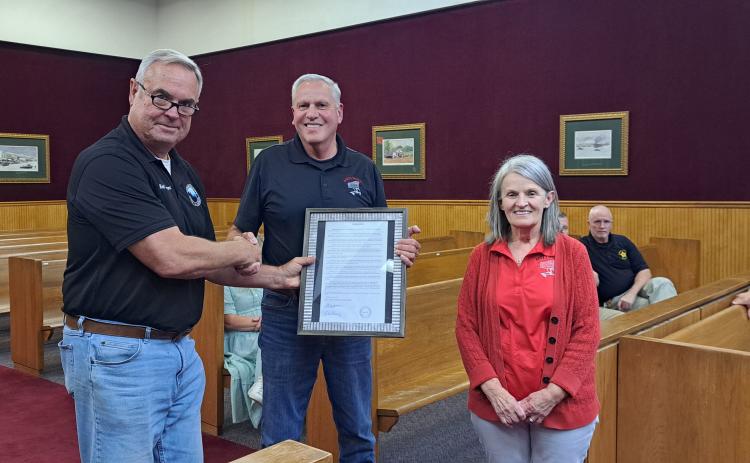 Megan Horn/The Clayton Tribune. Commissioner Kent Woerner, left, presents a Resolution to Andy and Deborah Hunter honoring them for the over 40 years of service that Andy’s Market gave to the community during the May 28 commission meeting. The local grocery store recently closed after decades.