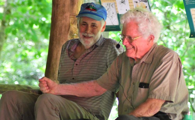 Enoch Autry/The Clayton Tribune. John Lane and Doug Woodward share a laugh at the picnic area at Warwoman Dell. Lane, an author, and Woodward, a former stuntman, told people at the event about the early days of the designation for the river. Left: Volunteer Jim Chance chops trees in the Warwoman Dell area as part of the early morning cleanup. Others walked trails picking up trash.