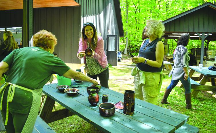 Enoch Autry/The Clayton Tribune. Kristin Mueller of Atlanta proudly shows her pottery to her sister Karin Mueller (right) at the Hambidge Center open house event on May 11. The U-Do-Raku activity was popular as pots were glazed and fired. Left: Christie Lyons and 13-year-old daughter Tricia Lyons of Lawrenceville work on their pottery at the open house. Tricia attends Hudgens Art School in Duluth.