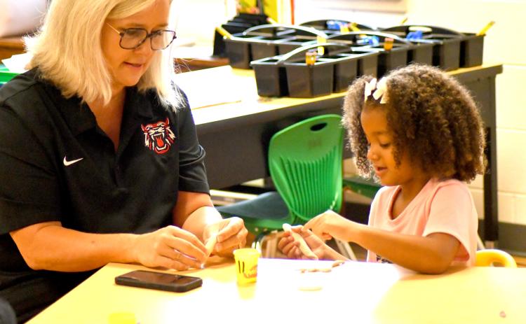 Enoch Autry/The Clayton Tribune. Superintendent Dr. April Childers assists kindergartener Emersyn Fuller with her clay on the first day of school on Tuesday, Aug. 6. Below: School Resource Deputy Sgt. Lindsey Owens directs school traffic on the first day Tuesday, Aug. 6.