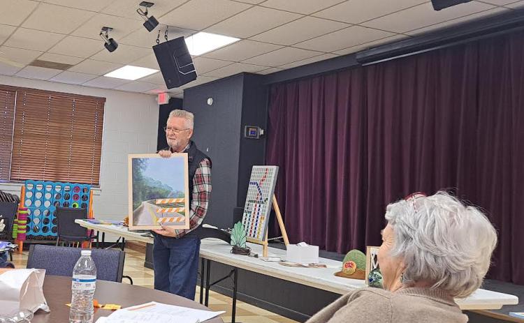 Megan Horn/The Clayton Tribune. Lewis Hinely showcases his artwork at the North Georgia Arts Guild members’ Show and Tell on Oct. 17. Hinely talked about how detours in artwork can be inspired by real life with this painting of a road detour sign. Guild member Kathy Ford is pictured in the forefront. Below:  Joey Aldrich-Burel presents her painting in pastels that was inspired by Vincent Van Gogh.
