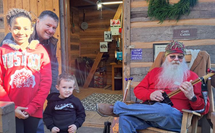 Megan Horn/The Clayton Tribune. Les Barnett of Mountain Man Music, right, demonstrates his panjo and canjo creations at Gott Cabin during “A Foxfire Christmas” on Dec. 7. Chris Adams, Kylee Curtis, 9, and Matthew Curtis, 3, learn a lot about instrument making from Barnett.