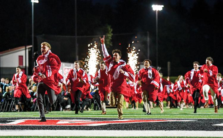 Wade Cheek/The Clayton Tribune. As sparks fly, the Rabun County High School Class of 2025 races to the victory bell at Frank Snyder Memorial Stadium, celebrating their completion of high school.