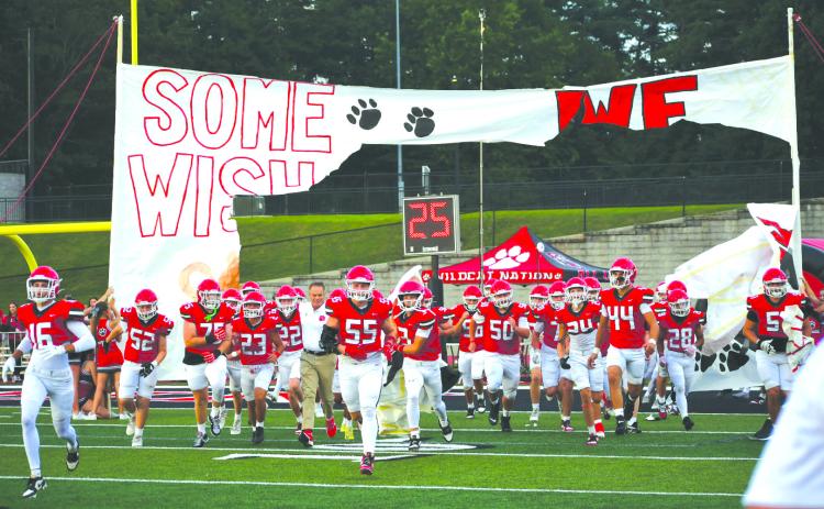 Enoch Autry/The Clayton Tribune. The Rabun County cheerleaders continued their tradition of creating special banners for each Wildcat football game so the team can run through them onto the football field. Here the players and first-year head coach Rance Gillespie (left center) make their way toward the home sideline during pregame of the Aug. 8 scrimmage against visiting Franklin, N.C.