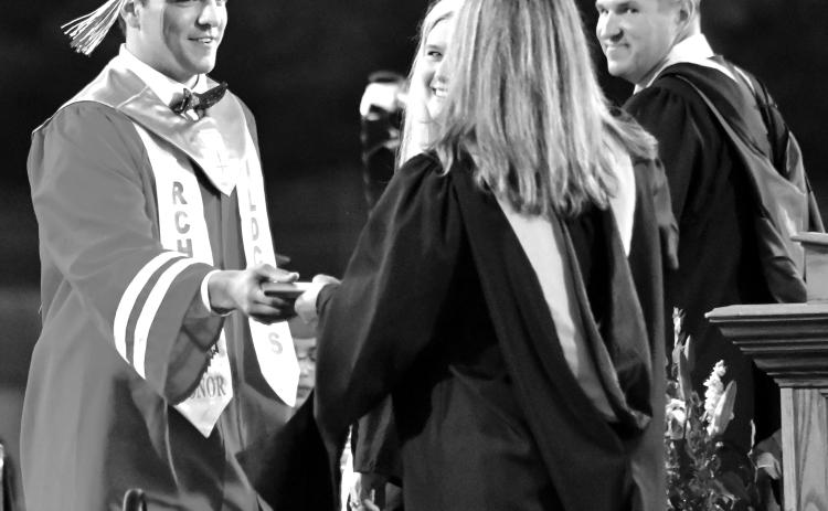 Enoch Autry/The Clayton Tribune. Rabun County High School Principal Justin Spillers (far right) and then Superintendent Dr. April Childers smile as Class of 2022 honor graduate and record-setting Wildcat quarterback Gunner Stockton receives his diploma in May 2022 from his mother Sherrie Stockton, then a RCHS counselor.