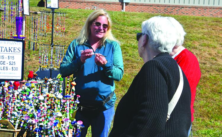 Enoch Autry/The Clayton Tribune. Danette Peters (center) of Why Knot Designs of Blairsville, Ga., talks with customers at the Nov. 1 Of These Mountains Fall MarketPlace on the Rabun County Civic Center Pavilions property. Why Knot Designs was one of the 120 booths that set a record for vendors at the event at the height of “Leaf Season.”