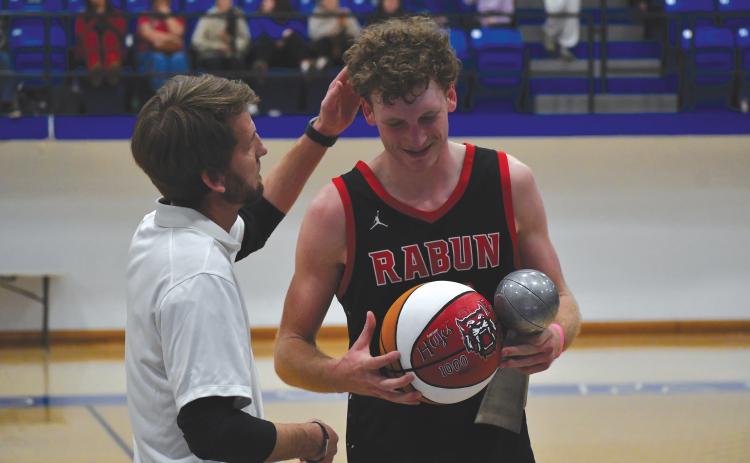 Wesley Branch/The Clayton Tribune. Rabun County boys head basketball coach David Adcock presents Hayes Free with a commemorative basketball for scoring his 1,000th point in his career in Rabun County’s 64-59 win over Chesnee (S.C.) in the championship game of the Battle of the States Tournament on Dec. 30. Free was also named MVP of the tournament and received the trophy that he is holding in the photo.