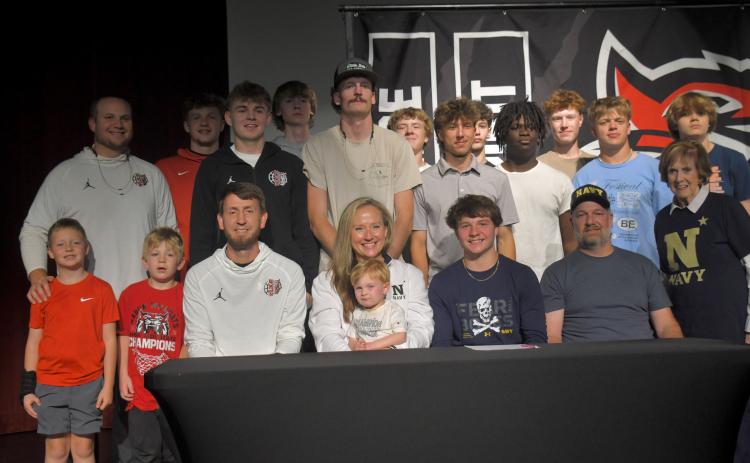 Wesley Branch/The Clayton Tribune. Rabun County senior Huey Blalock (center, right) poses with his family and the RCHS boys basketball team after signing his letter of intent to Navy on April 30 at the Rabun County High School Fine Arts Building. Blalock led the Wildcats to their first ever state title this season.