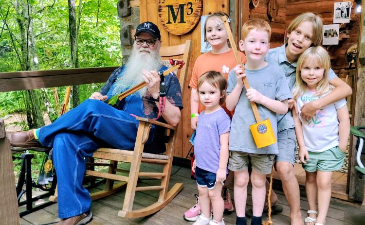 Megan Horn/The Clayton Tribune. Les Barnett with Mountain Man Music Custom Guitars showcases his unique panjos and canjos to kids at Foxfire Heritage Days. Barnett demonstrates his musical instruments to Chesney Godwin, 8; Tio O’Connell, 10; Astra O’Connell, 4; Emmy Kate, 2; and Henry Godwin, 5.
