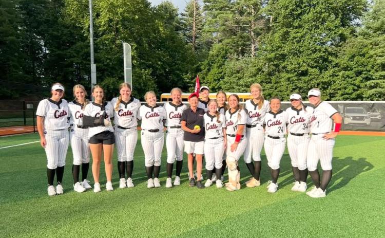 Submitted Photo. Former Rabun County High School teacher and coach Janice Wayne (center) poses with the Rabun County softball team after throwing the first pitch at a game during the 2025 season. Wayne, the first-ever softball coach at RCHS who also assisted athletics in a plethora of ways, passed away on June 24 at the age of 72. 