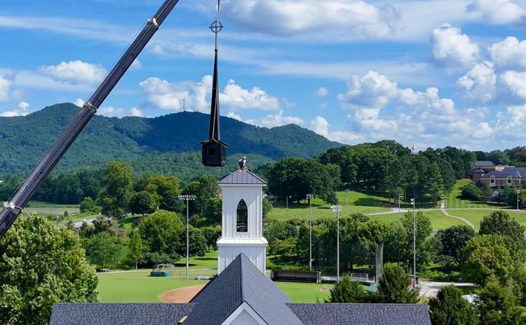 Photo courtesy Scott Poss.  A crane from TKS Installation and Sales of Warner Robins, Ga., lifts the new steeple and spire to the belfry tower of the new sanctuary of Rabun Gap Presbyterian Church. Chuck Lanier perches atop the tower to guide it in place. In the background is the Rabun Gap Nacoochee School, where the church first met in 1929.