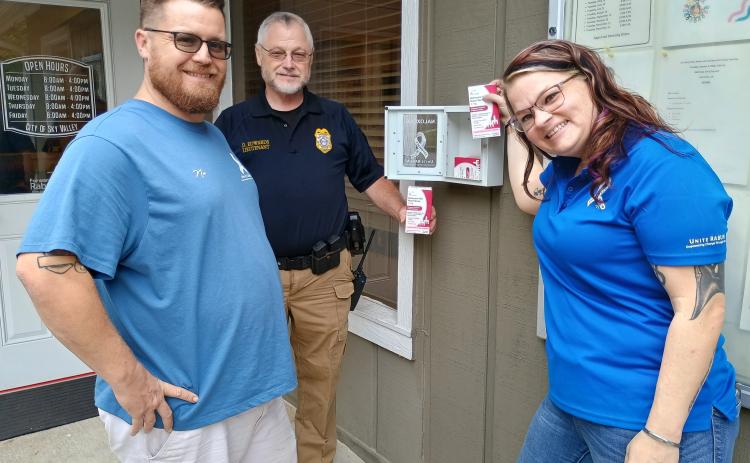 Megan Horn/The Clayton Tribune. Nic Huber, Peer Support Specialist for Unite RABUN, left; Sky Valley Police Department Lt. David Edwards; and Unite RABUN Executive Director and Peer Support Specialist Brittany Roquemore install an “Overdose Emergency Kit” equipped with Naloxone at Sky Valley City Hall on Oct. 5. They installed six kits at five different locations in the City of Sky Valley.