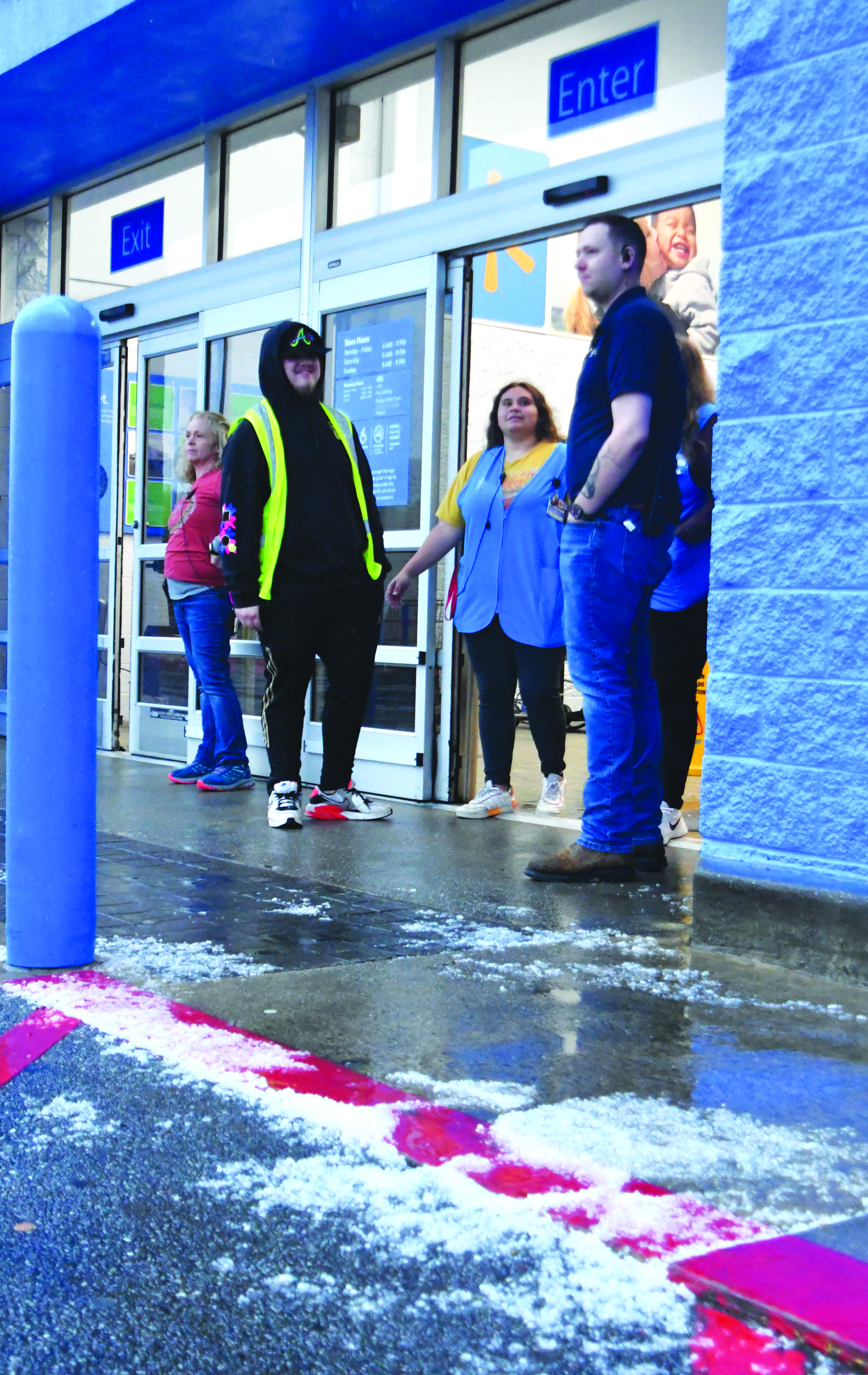 Enoch Autry/The Clayton Tribune. With piles of nickel-sized hail on the ground, Carl Brown (right), Clayton Walmart front-end coach, stands outside with fellow store employees to inform entering customers those inside have been urged to go to the back of the store due to the risk of a tornado.