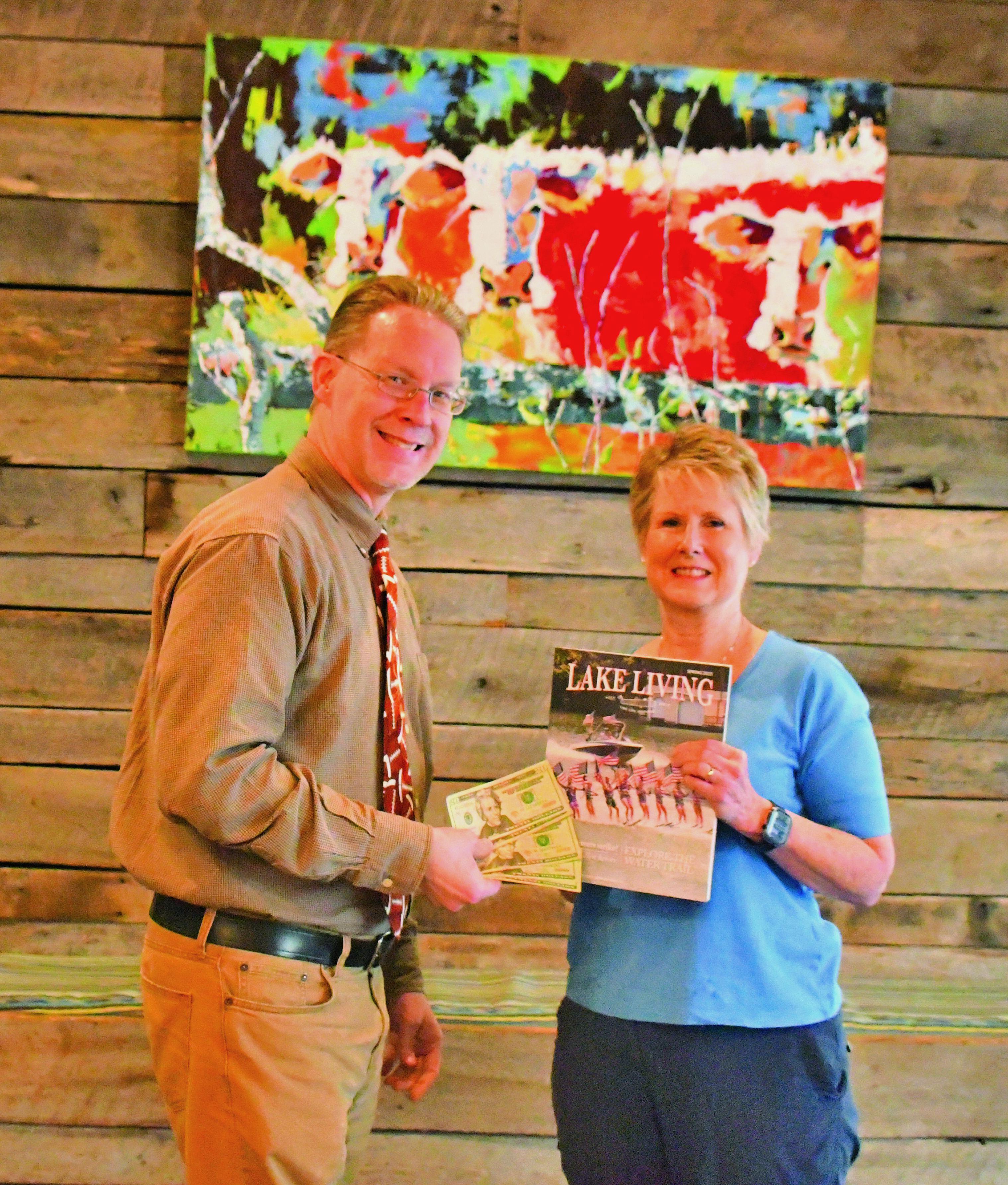 Megan Broome/The Clayton Tribune. Enoch Autry, publisher for The Clayton Tribune in Rabun County, presents the $100 prize to Rabun County resident Melissa Elzey for winning the Spring 2023 Lake Living cover contest with her capture of the Lake Burton Ski Patriots’ performance on July 4, 2021. 