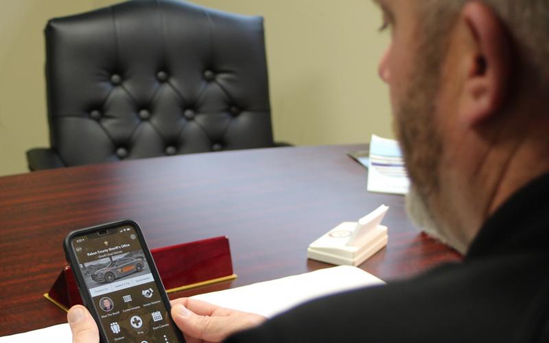 Megan Broome/The Clayton Tribune. Rabun County Sheriff Chad Nichols looks over the new phone app his department recently released to the public. 