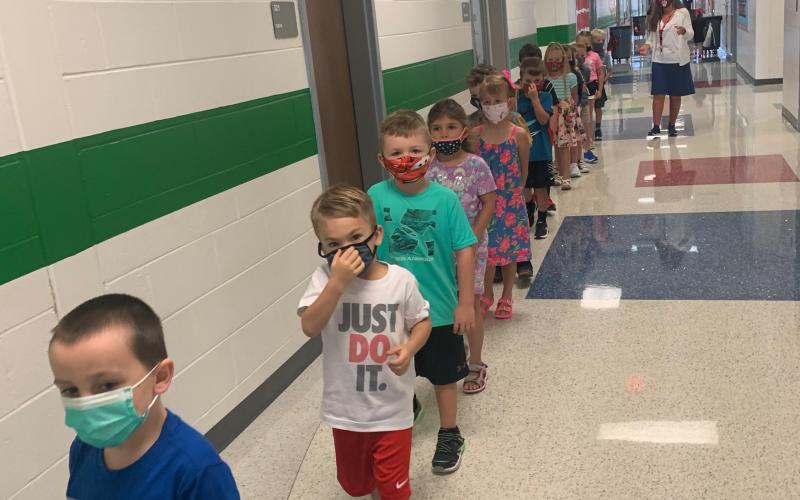Photo courtesy Rabun County Schools. Jax Jackson, left, Asher Justice, Jordan Whipple and Kasi Jai Blalock from Mrs. Moore’s kindergarten class stand single-file in the hallway wearing masks during the first week of school as part of COVID-19 safety measures in the school system. One-direction hallways are part of the “new normal” for the school year. 