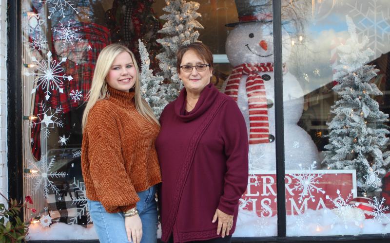 Megan Broome/The Clayton Tribune. Madison Hall, left, owner of Madison’s on Main in Clayton, and employee Carol Cott stand in front of the shop’s window on Monday, which won first place in the window decorating contest. 