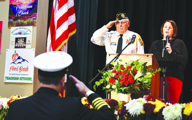 Megan Broome/The Clayton Tribune. Veteran Doug Wayne and fellow soldiers salute the American Flag as Lora Burrell sings The Star-Spangled Banner at the opening of the Veterans Appreciation Dinner held at the Rabun County Civic Center. 