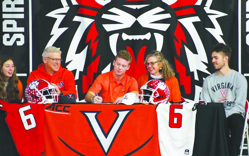 Luke Morey/The Clayton Tribune. Surrounded by his family, senior wide receiver Jaden Gibson (center) signs his letter of intent with Virginia on Wednesday, Dec. 21. The other Gibsons on the stage include from left, Janakate, Jason, Jennifer and Jasper.