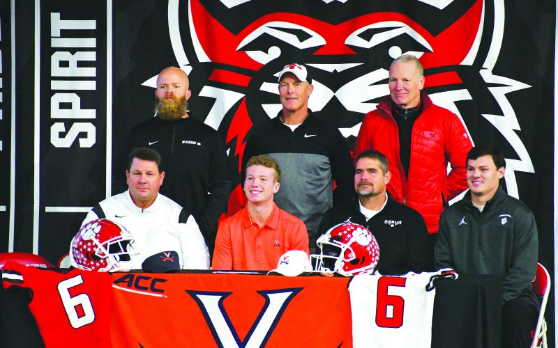 Luke Morey/The Clayton Tribune. Rabun County’s three-star wide receiver Jaden Gibson (middle) signed his letter of intent to play collegiately at the University of Virginia on Wednesday, Dec. 21. Gibson is joined by football coaches from top left, Caleb Bagley, Tim Corbett, David Rodgers, Michael Davis, Ricky Ross, and Wes Holcombe. Additional photographs from Gibson’s signing ceremony can be found on The Clayton Tribune’s website. 