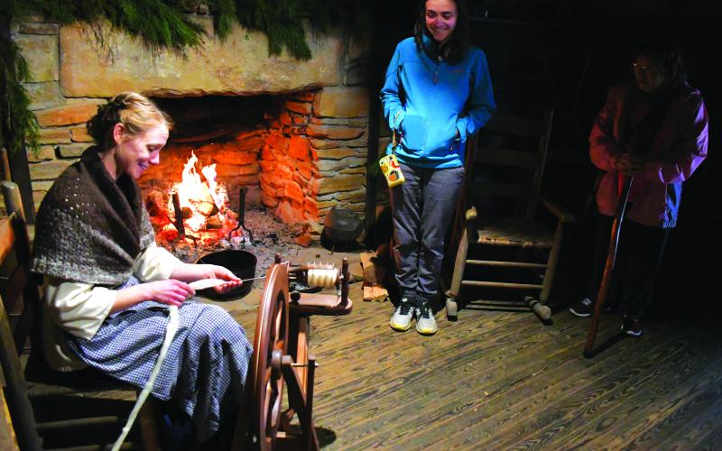 Enoch Autry/The Clayton Tribune. Foxfire Assistant Curator Kami Ahrens offers information to the public as she operates a spinning wheel in the Savannah Cabin on the museum’s Mountain City property on Dec. 10 during a Foxfire Christmas.
