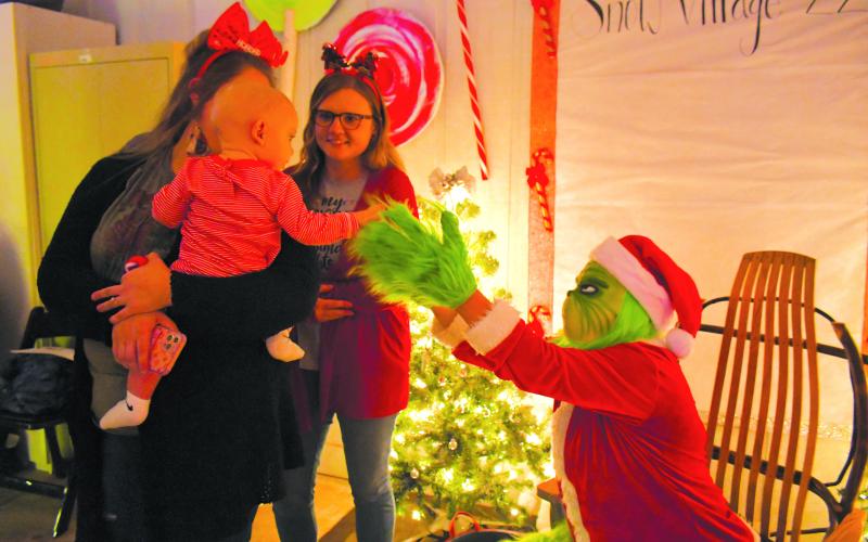 Megan Broome/The Clayton Tribune. Nine-month-old Holton Morgan shakes hands with The Grinch at the Christmas Village of Lights display on Dec. 10. Also pictured are Kelsey Taylor and Irene Sheppard with FAITH.