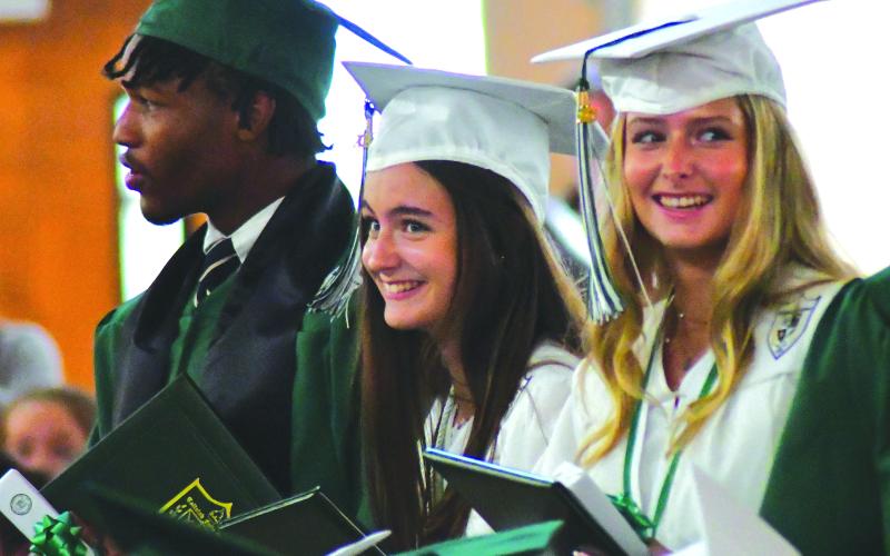 Enoch Autry/The Clayton Tribune. With fellow graduate Frankey Moree, Tallulah Falls seniors Meredith Morris and Madeline Mullis share a laugh during the May 19 ceremony.