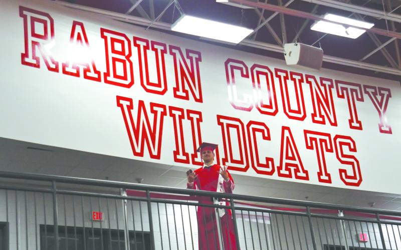 Enoch Autry/The Clayton Tribune. Noah Legault stands in front of the Rabun County Wilcats sign in the gymnasium as he looks down toward his classmates on the floor before the seniors head to Frank Snyder Memorial Stadium.