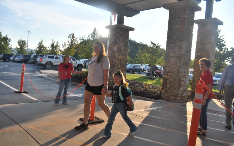 Megan Broome/The Clayton Tribune. First Grade student Katie Hopper walks to school for the first day of class with mom Kayla Smith. Below:RCES student Reese Dean selects the book “Ranger In Time” from the school library.