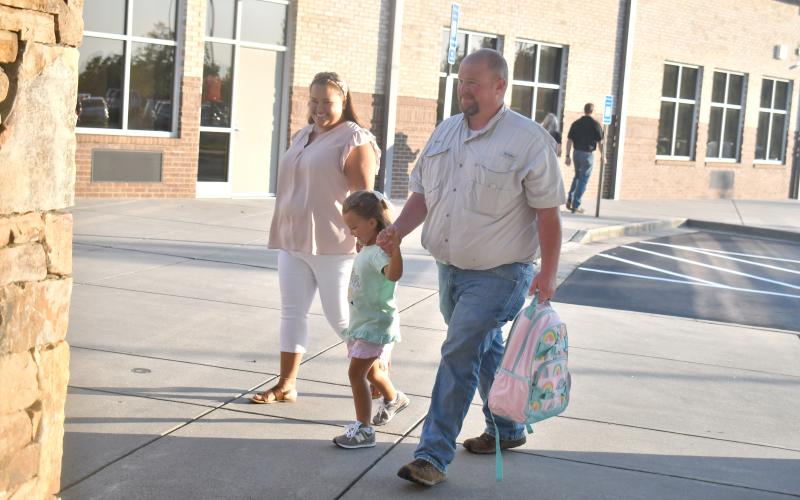 Megan Broome/The Clayton Tribune. Kindergartener Ada Nichols walks to RCPS on the first day of school with parents Brittney and Joshua Nichols. Below:RCES student Reese Dean selects the book “Ranger In Time” from the school library.