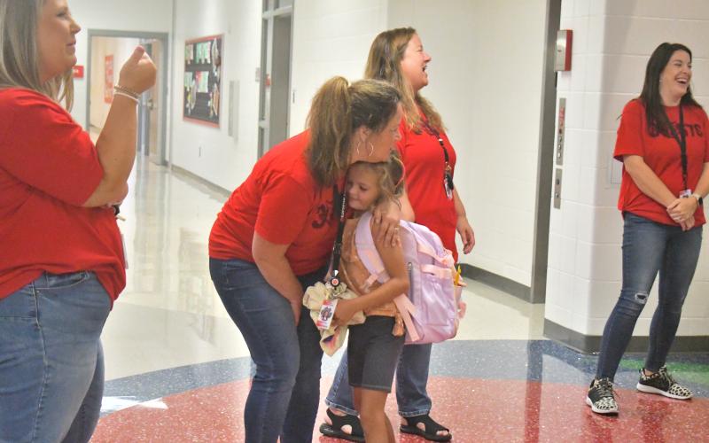 Megan Broome/The Clayton Tribune. Pre-K teacher Mrs. Cynthia Hulsey gets a hug from First Grader Reeves Bragg on the first day of school at RCPS. Below:RCES student Reese Dean selects the book “Ranger In Time” from the school library.