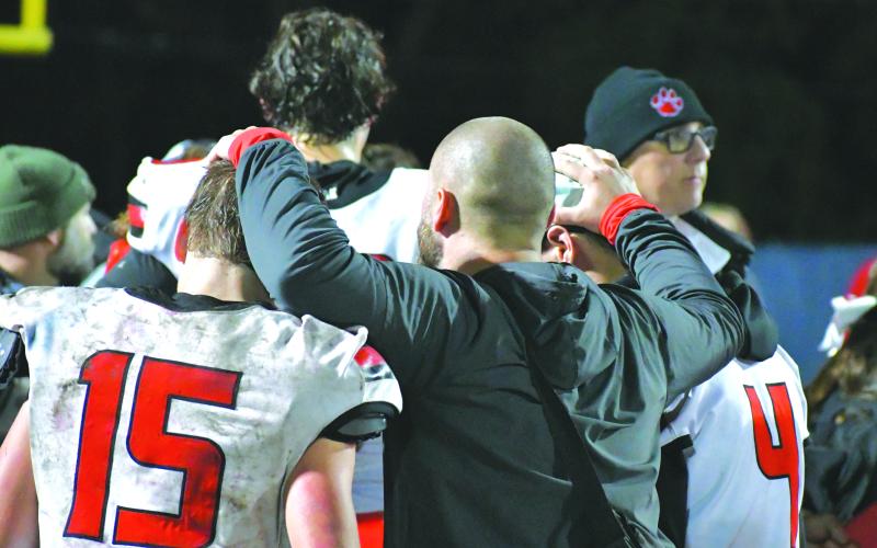 Wade Cheek/The Clayton Tribune. Rabun County assistant coach Clay Worley rests his hands on the top of the heads of Reid Giles (15) and Noah English (4) who played on offense and defense for the Wildcats during the 2023 season. The Trojans would defeat the Wildcats 39-13 in the game to move on in the state playoffs.