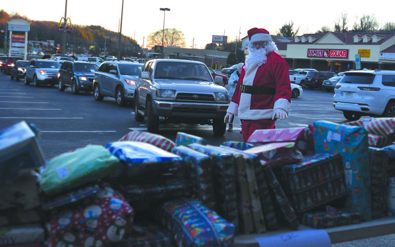 Enoch Autry/The Clayton Tribune. Santa takes a look at the tables filled with presents as a string of vehicles wraps around the parking lot in the background.