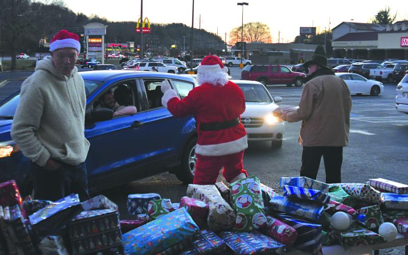 Enoch Autry/The Clayton Tribune. Santa takes a look at the tables filled with presents as a string of vehicles wraps around the parking lot in the background.