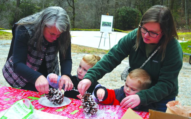 Enoch Autry/The Clayton Tribune. Laura Blackwell (from left) helps Hayes Blackwell while Haylei Cross assists Connor Cross decorating large pine cones at “A Foxfire Christmas” in Mountain City. Left: Kim Cannon from the Rabun County Public Library read a variety of books that depicted pioneer life in the Appalachian Mountains on the Shooting Creek Cabin porch.