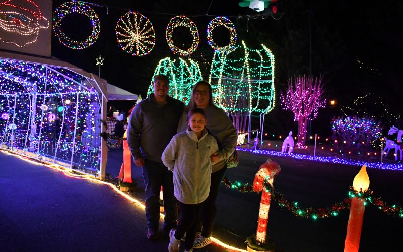 Megan Horn/The Clayton Tribune. Kenneth, Jacqueline and Macey Frady pose for a photograph in front of some of the many lit decorations at the event in Tiger. Left: Five-year-old Ethan Moseley hugs The Grinch at the Village of Lights.