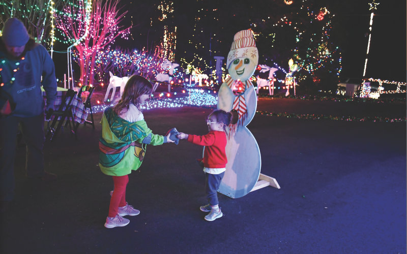 Megan Horn/The Clayton Tribune. Jane Harris, 7, and Raylen Dula, 3, throw snowballs into the snowman on Dec. 8 at the 10th Annual Christmas Village of Lights. Left: Five-year-old Ethan Moseley hugs The Grinch at the Village of Lights.