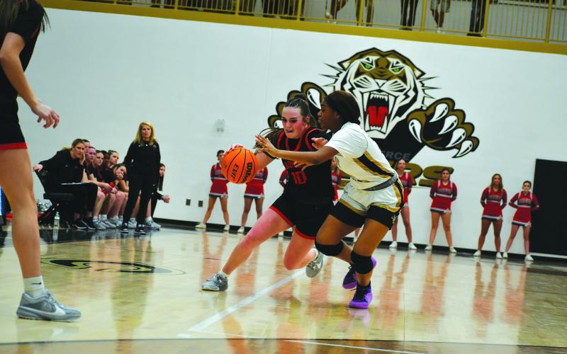 Wade Cheek/The Clayton Tribune. With Lady Cat head coach DeeDee Dillard, the RCHS players, and RCHS cheerleaders watching, senior Mili Watts makes her move to the basket against the Lady Tigers in Commerce.