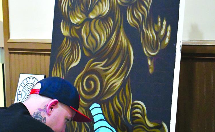 File Photo Enoch Autry/The Clayton Tribune. Artist Matthew Robertson paints background blue spirals on his Bigfoot rendering he created at the 2022 Georgia Bigfoot Conference in Clayton at the Rabun County Civic Center. This year’s popular event will be held on April 1 at The Dillard House.