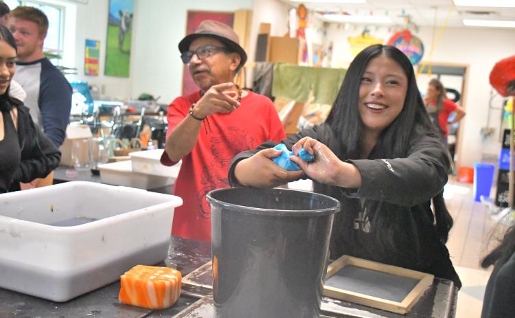 Megan Broome/The Clayton Tribune. Student Camila Gaspar smiles as she hand makes paper with guest artist Javier Silverio onlooking in the Rabun County High School art room April 21. Gaspar squeezes a sponge to make paper just as Silverio does at Taller Leñateros in Chiapas, Mexico.